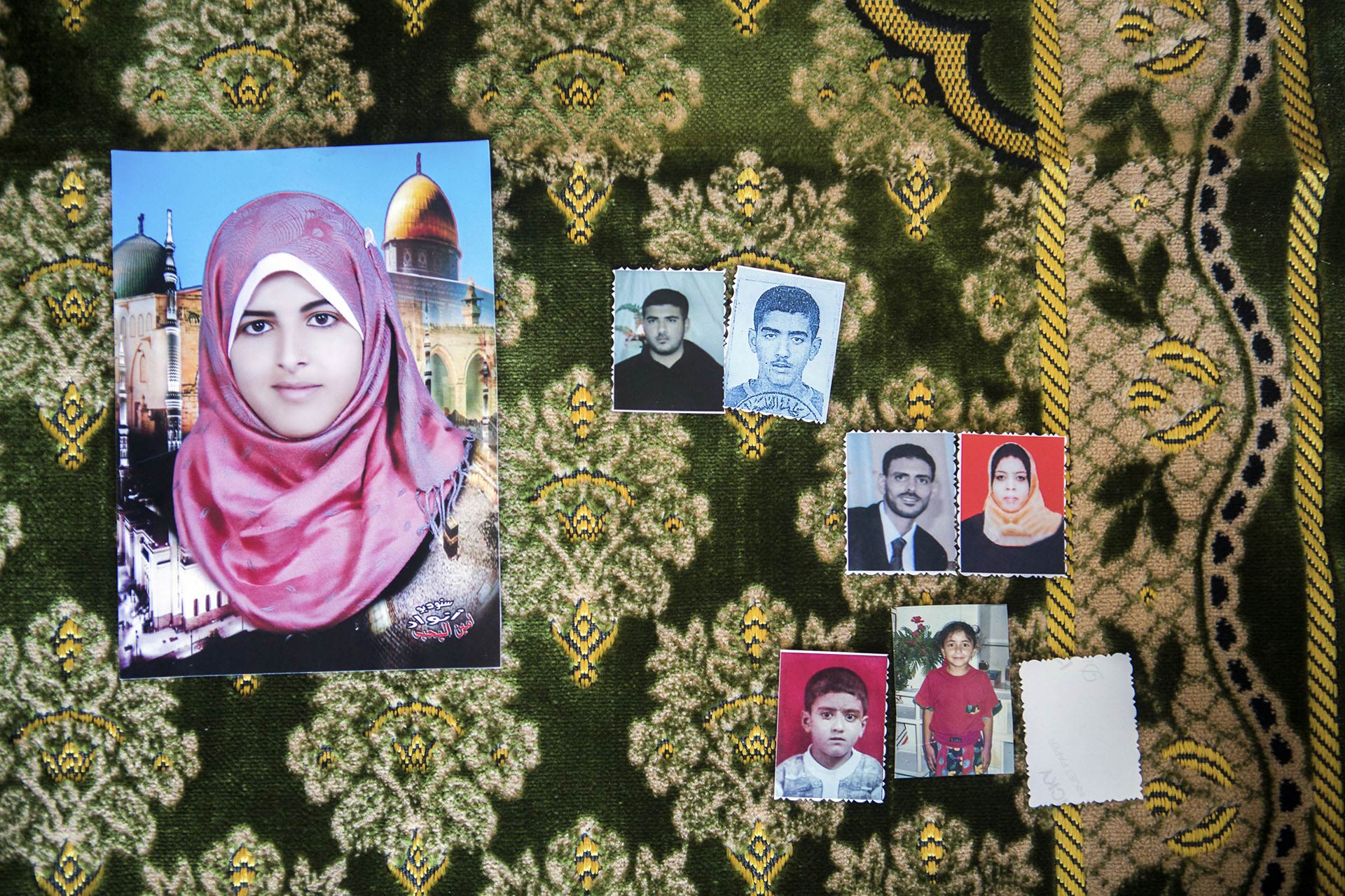 Photos des sept membres qui furent tués de la famille Al-Louh, étalées sur le tapis de prière d’Iman al-Louh. Iman priait sur ce tapis lorsqu’elle fut frappée par un morceau de béton qui vola au travers de sa fenêtre de chambre.  
